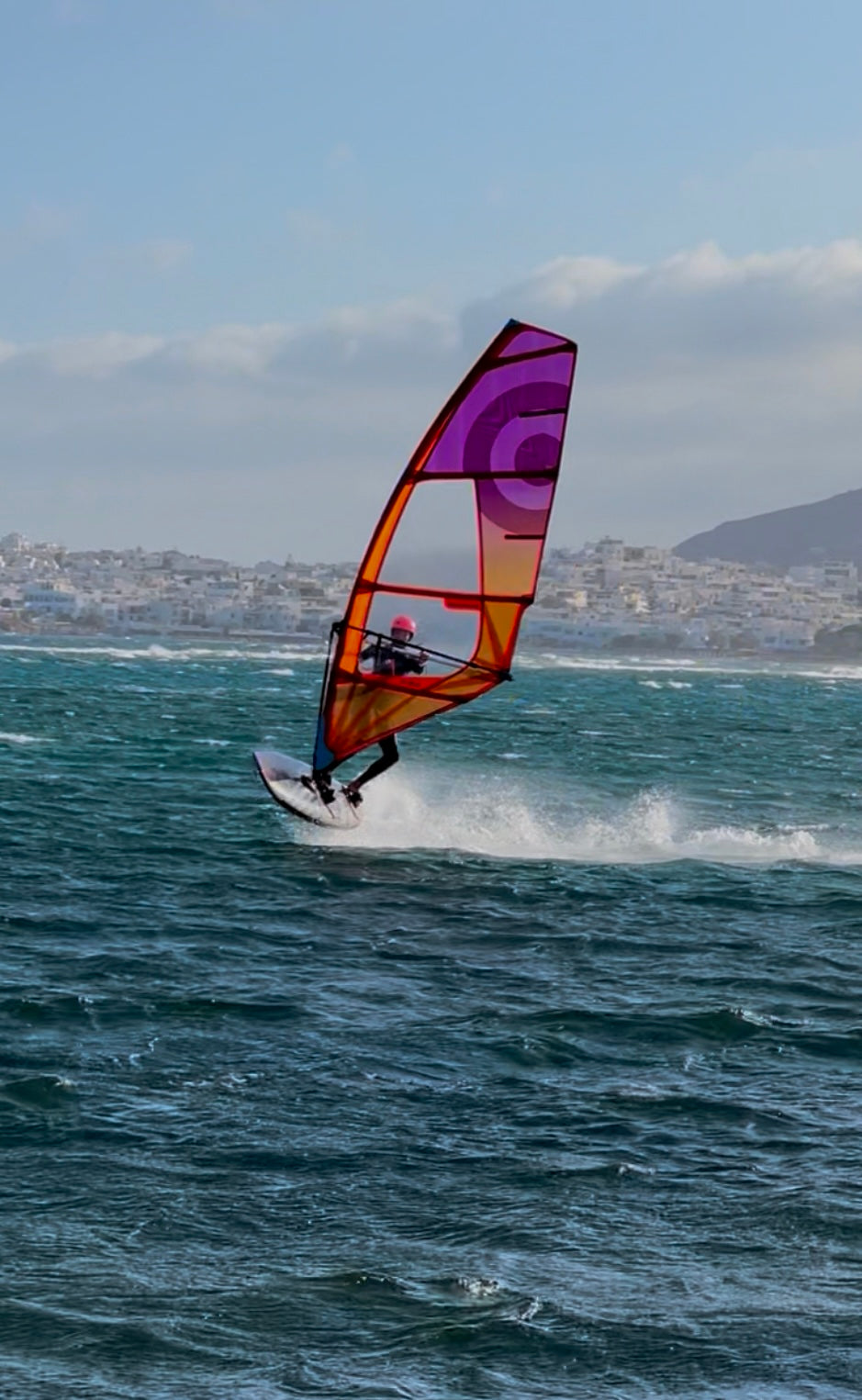 Gekleurd zeil, windsurfer sprint, blauw water, stad op achtergrond, blauwe lucht. 