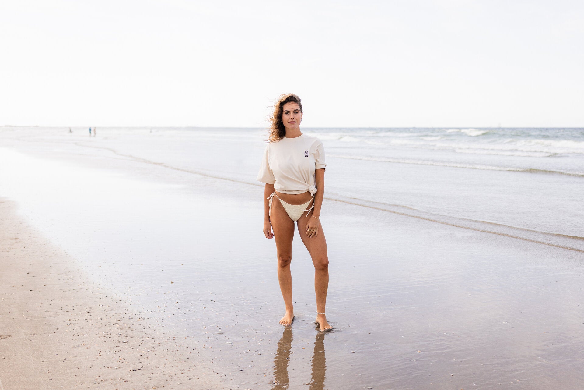 Vrouw in bikini op het strand, met een opgeknoopt T-shirt. 