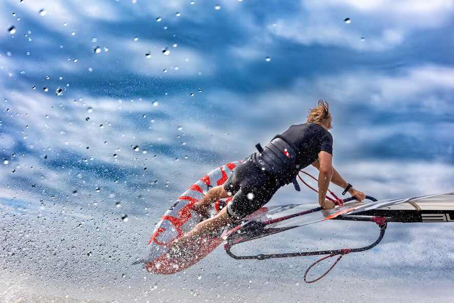 freestyle windsurfer, rood met wit hard, zwart wetsuit, zwarte trapeze, jongen met blond haar, blauwe lucht met wolken