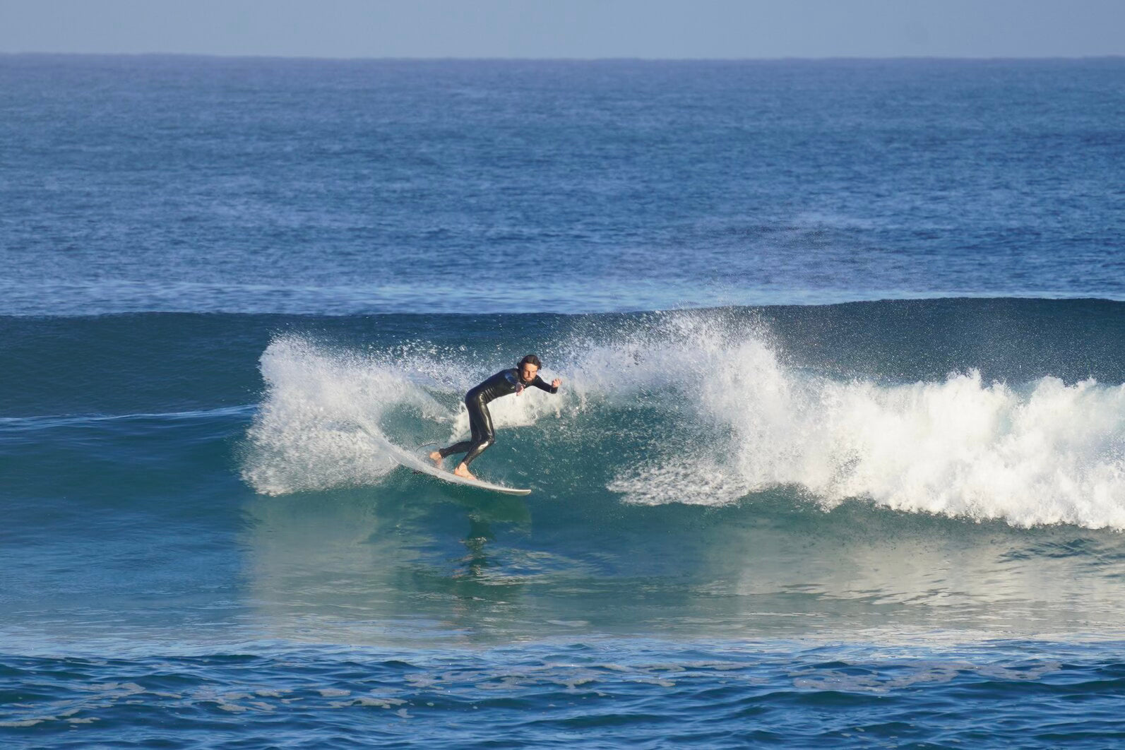 Golfsurfer, grote golf, blauw water, jongen, zwart wetsuit.