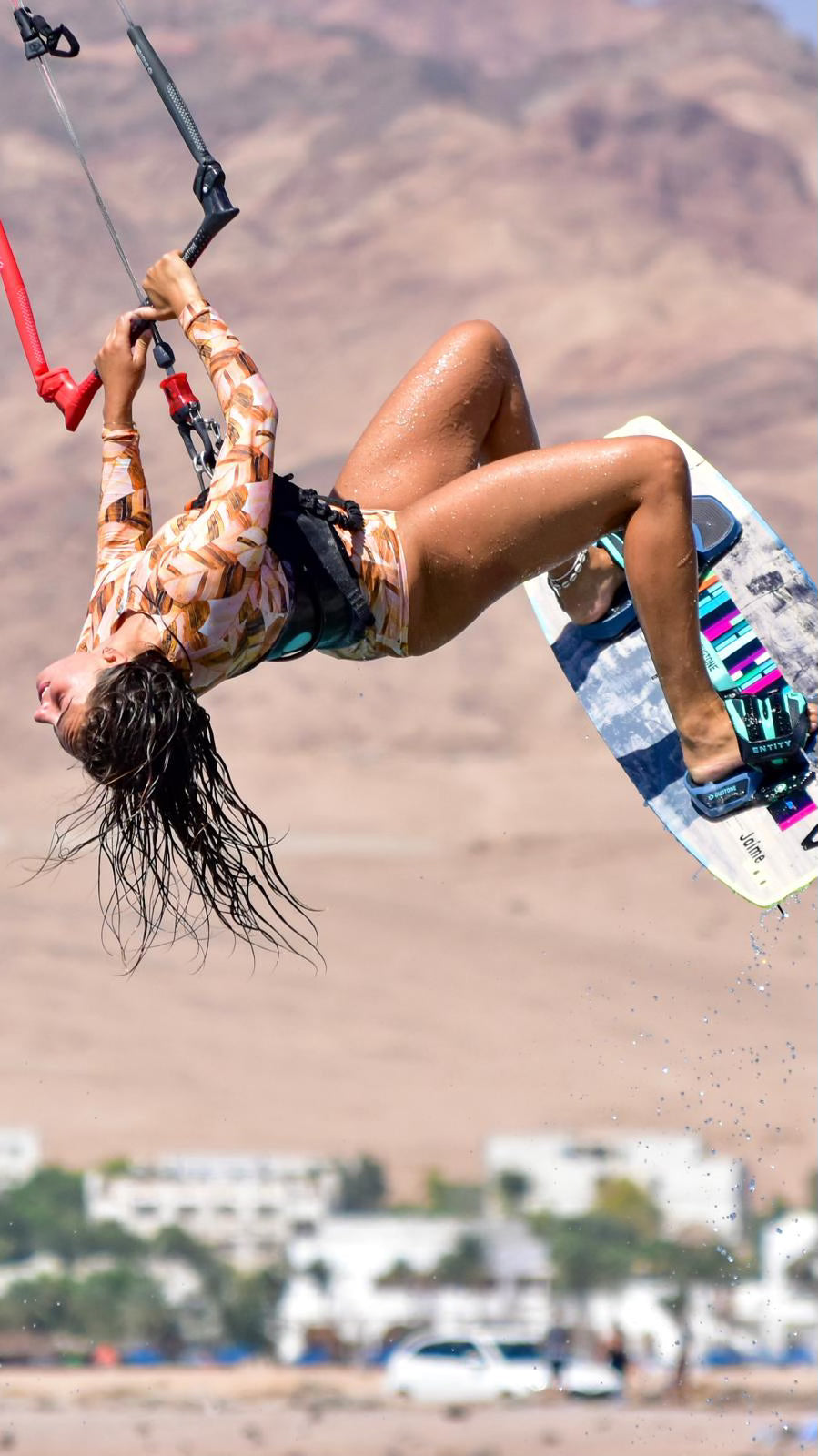 vrouwelijke kitesurfer, gekleurd badpak, bruine lange haren, hoge sprong, bergen